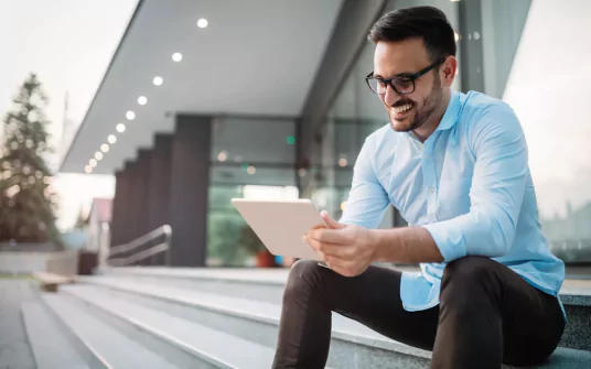 A man in glasses and a blue shirt smiling at a tablet