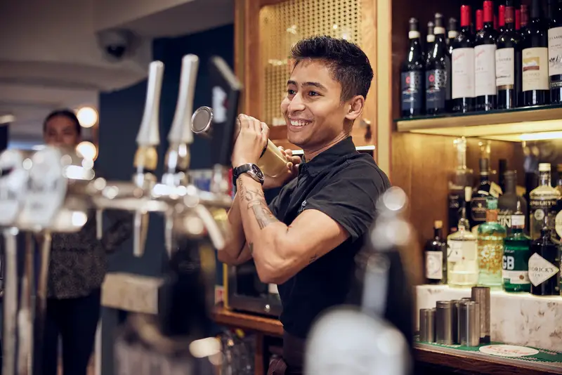 Barman in a black shirt shaking a cocktail in a shaker behind a bar