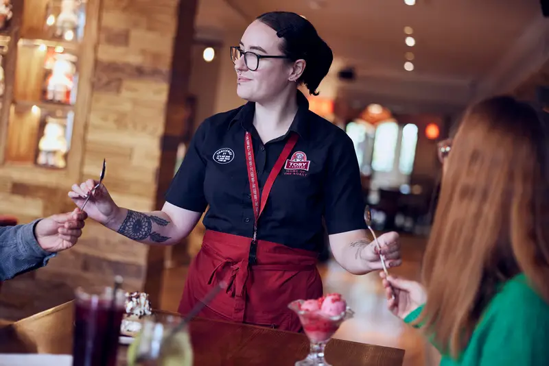 Barman in a black shirt shaking a cocktail in a shaker behind a bar