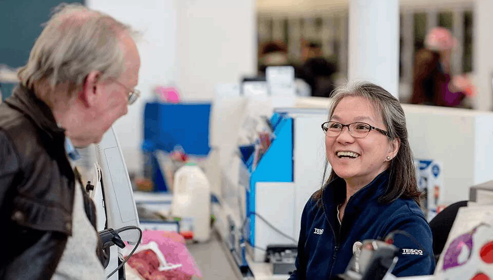 A customer being served at a till. the customer and till operator are smiling at eachother